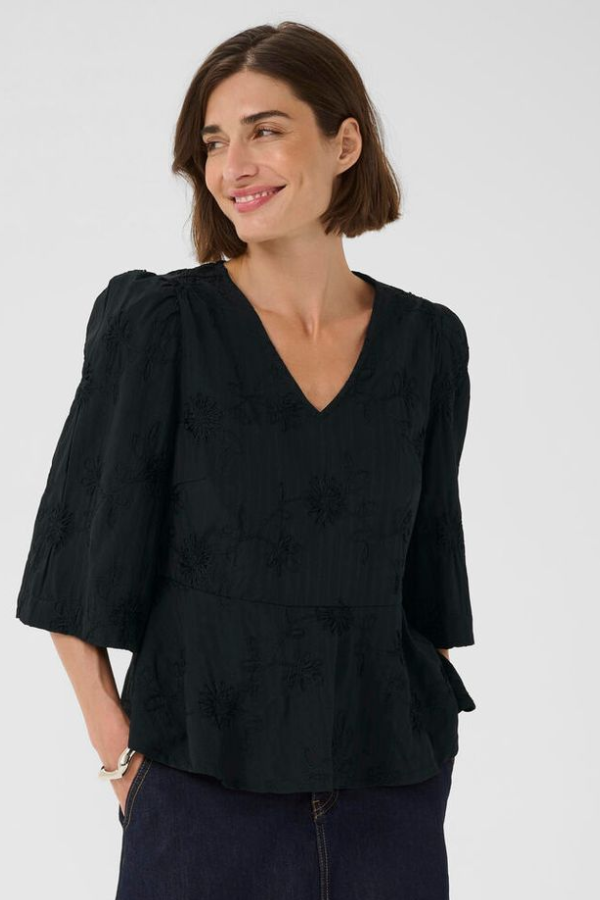 Woman wearing a black blouse with puff sleeves and embroidered florals against a white background