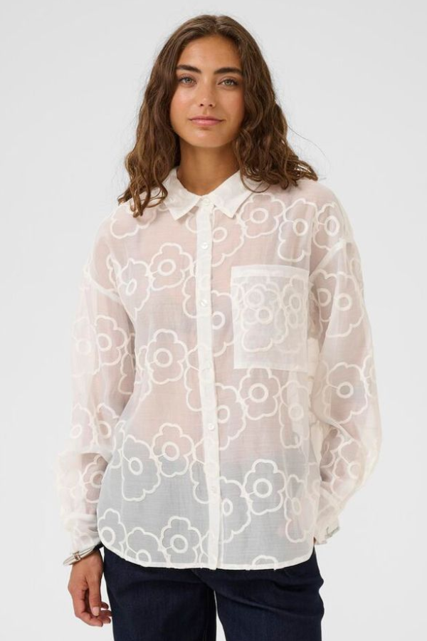 Woman wearing a sheer white floral blouse with a plain background