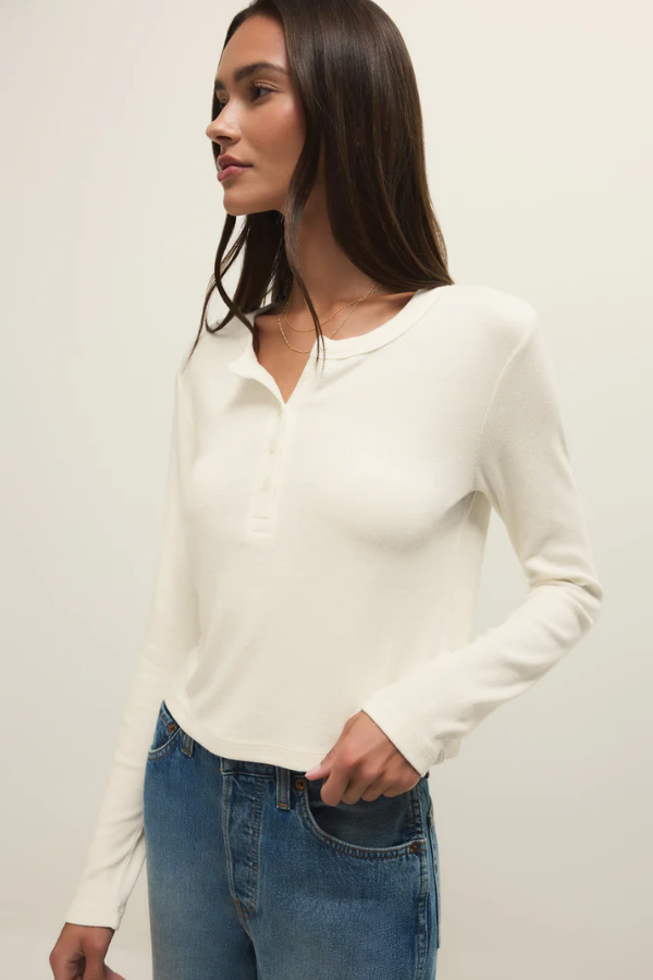 Woman wearing a white long-sleeve top and blue jeans against a plain background