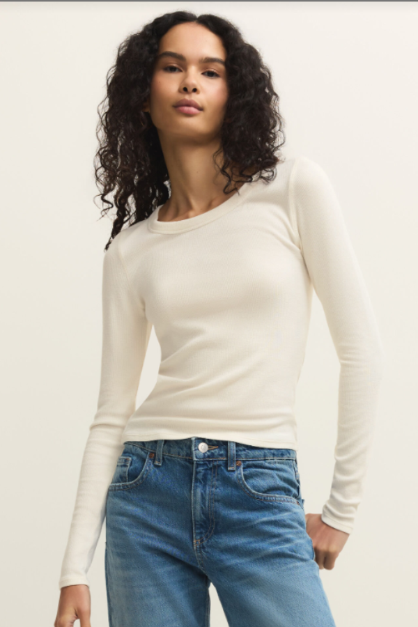 Woman wearing a white long-sleeve top and blue jeans on a plain background