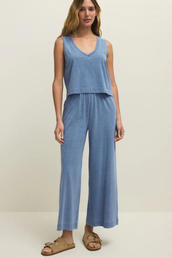 Woman wearing a blue sleeveless top and wide-leg pants on a plain background