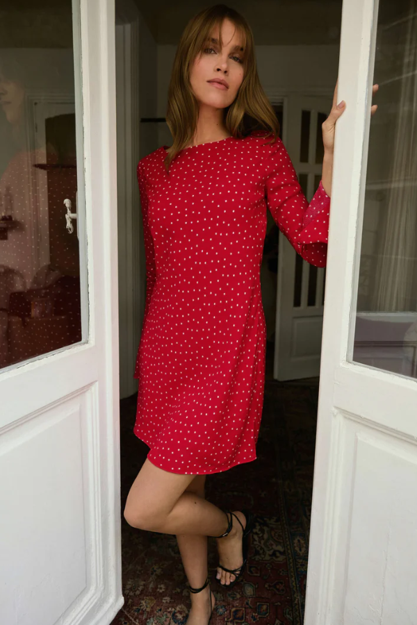 Woman in a red polka dot dress standing in a doorway.